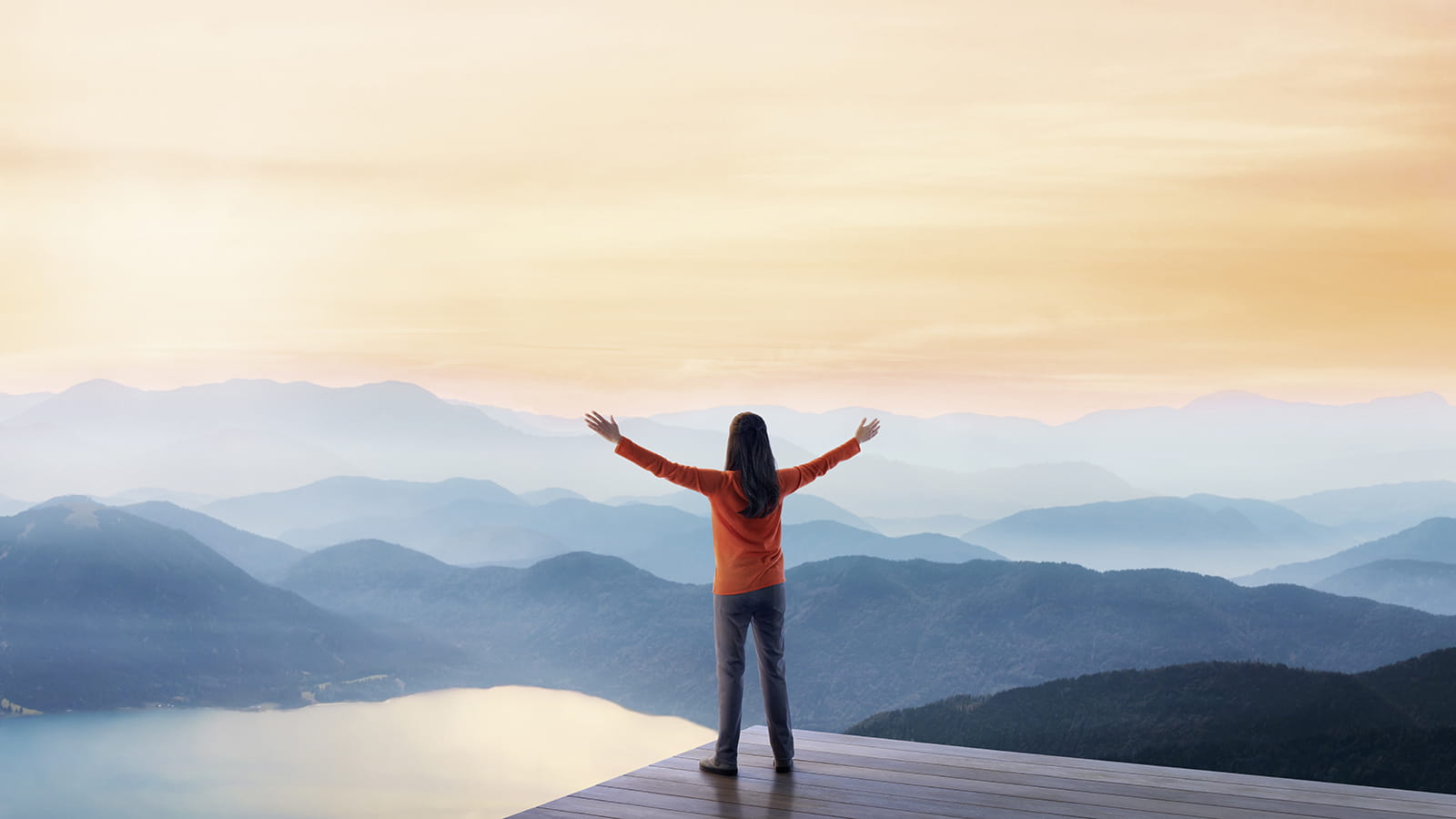 Woman with arms outstretched looking at a mountainous landscape
