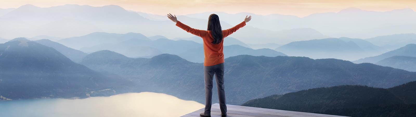 Woman with arms outstretched looking at a mountainous landscape